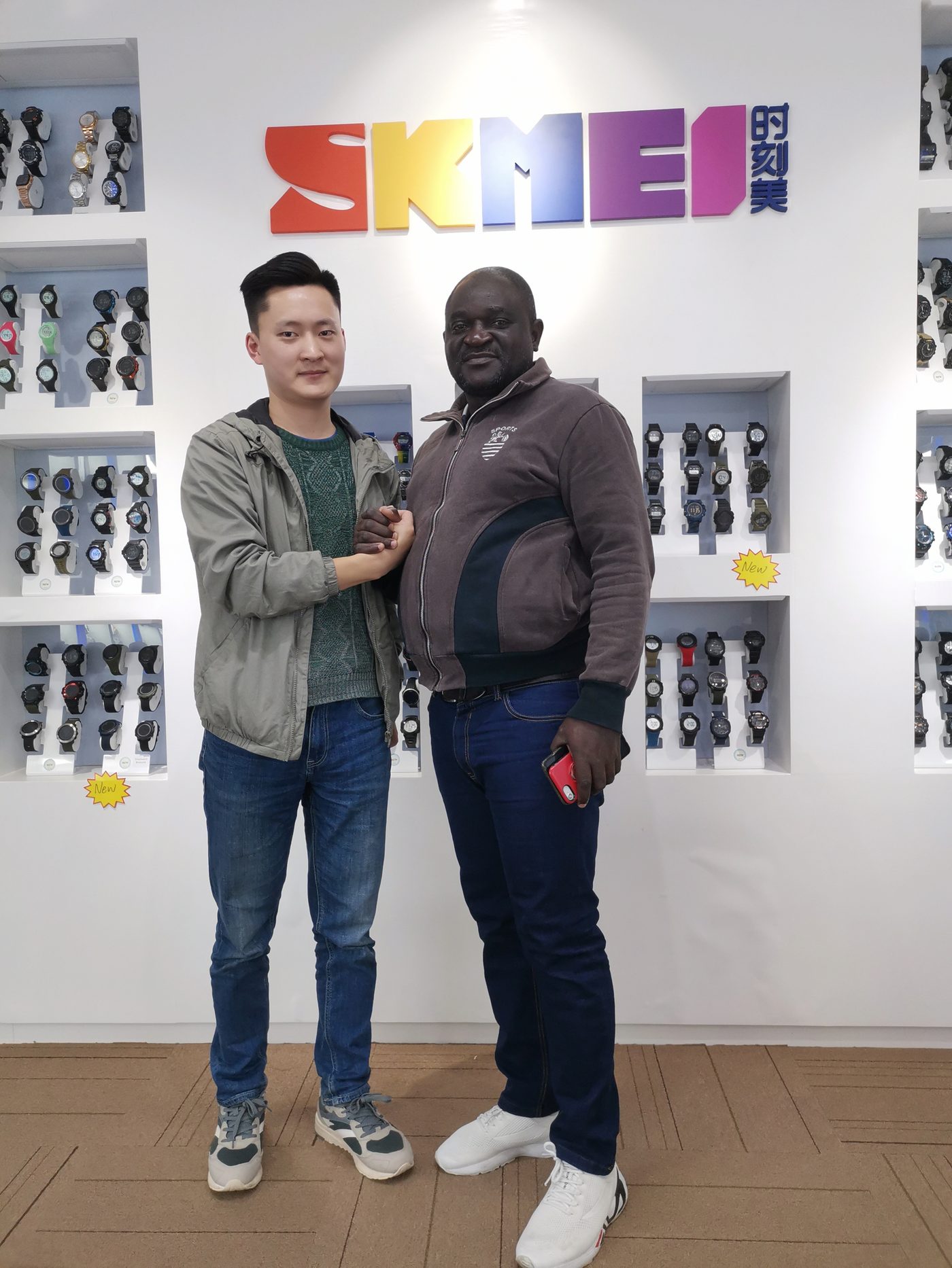 Overseas customer shaking hands with a SKMEI representative in front of the sample wall, December 2019