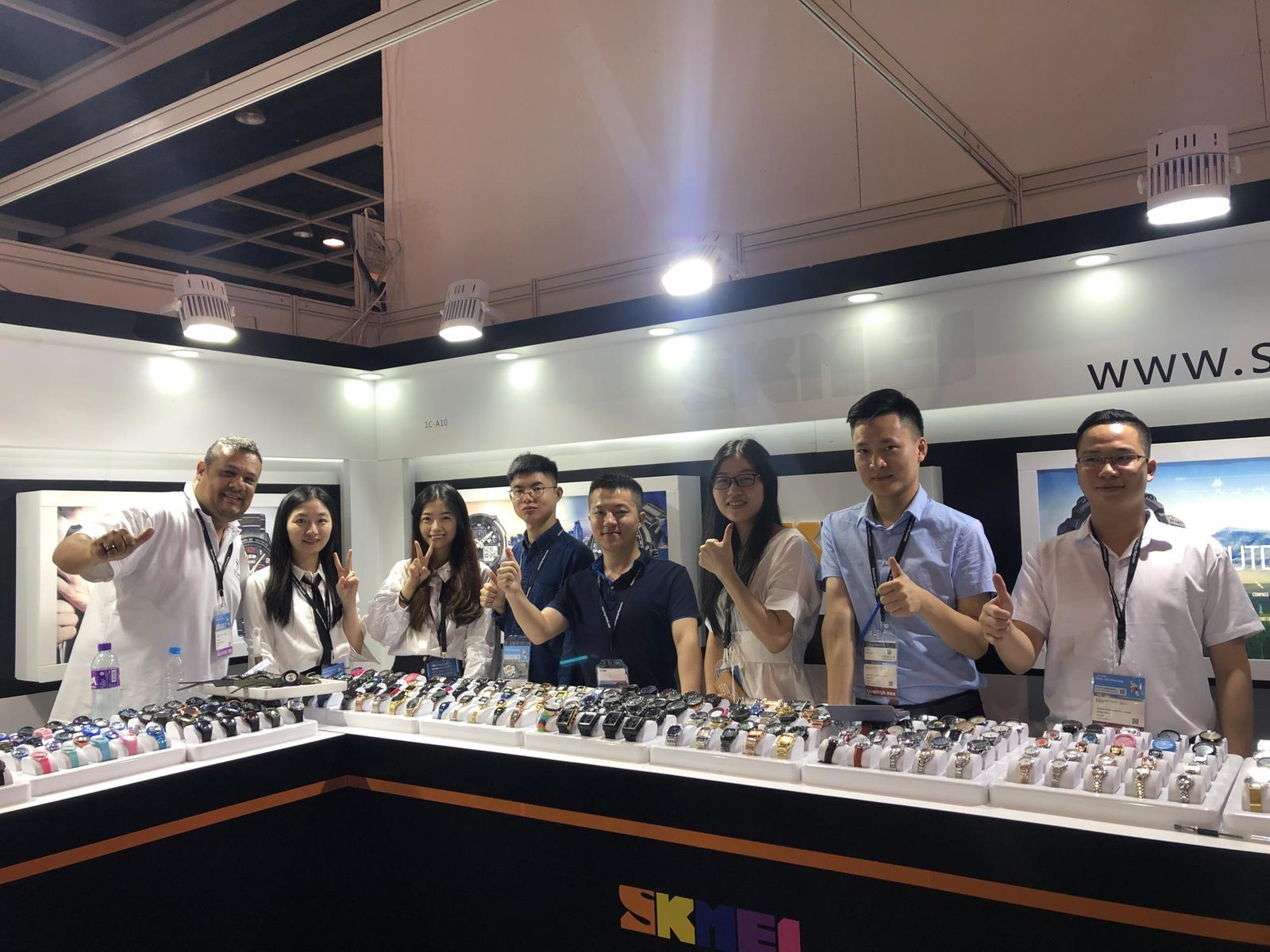 SKMEI team and an international visitor behind the watch counter at the 2019 Hong Kong trade show booth
